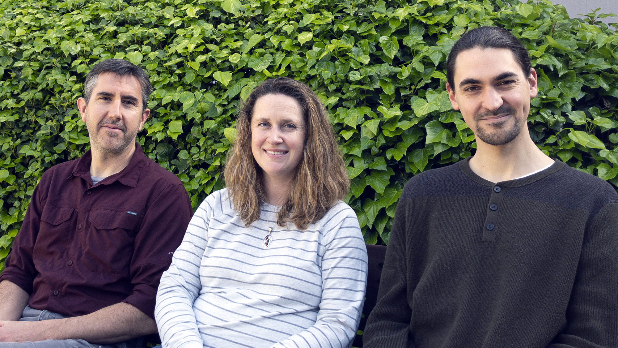 Three researchers sit against a leafy backdrop.