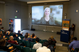 people in an auditorium watching someone talk on a projector