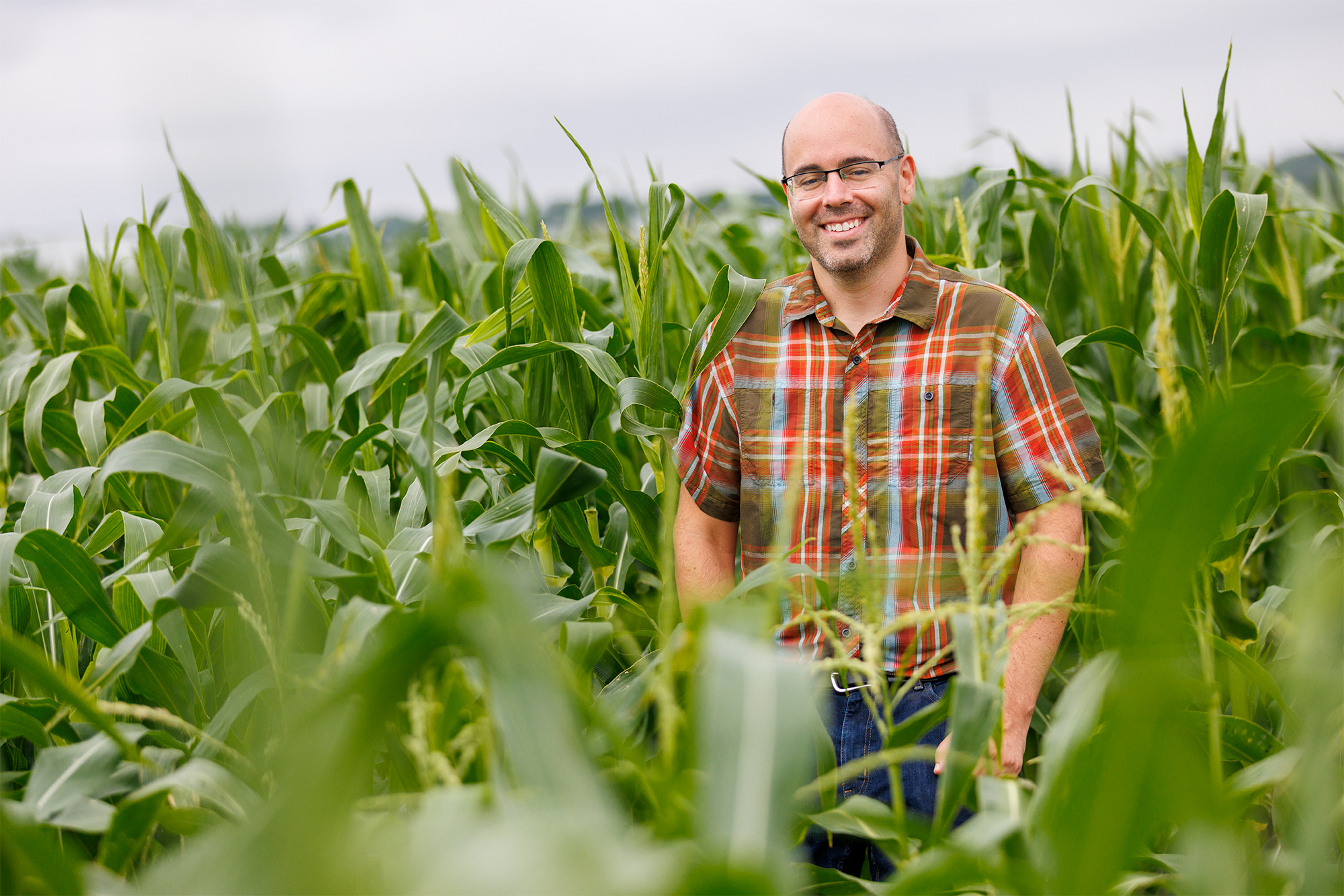 A scientist in glasses smiles in a field of corn.