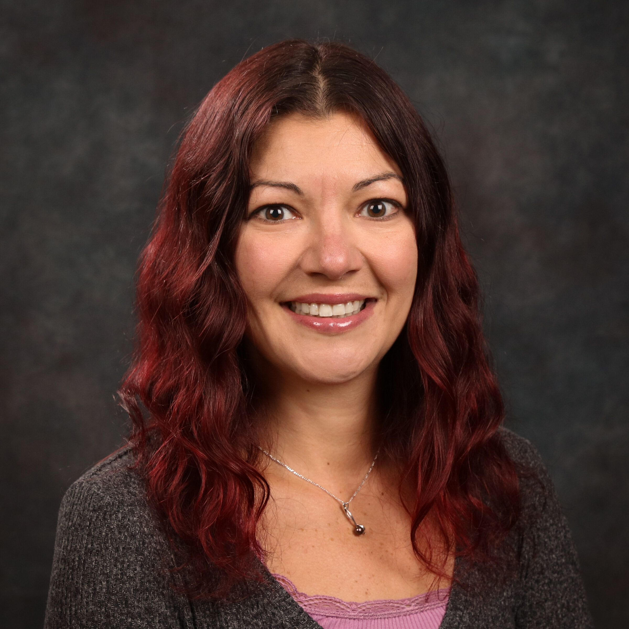an individual with long red hair wearing a gray cardigan over a pink top