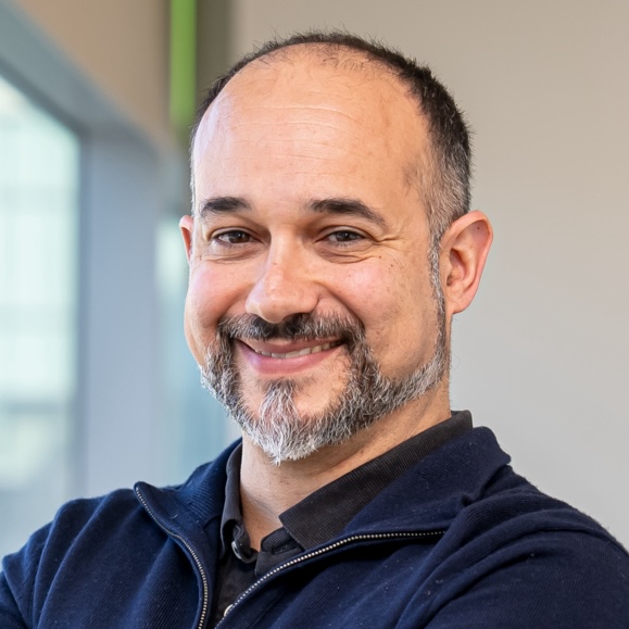 An individual with short hair, a mustache and beard wearing a navy blue shirt