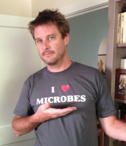 a person with a shirt that says "I heart microbes". a hand is under the sentence.