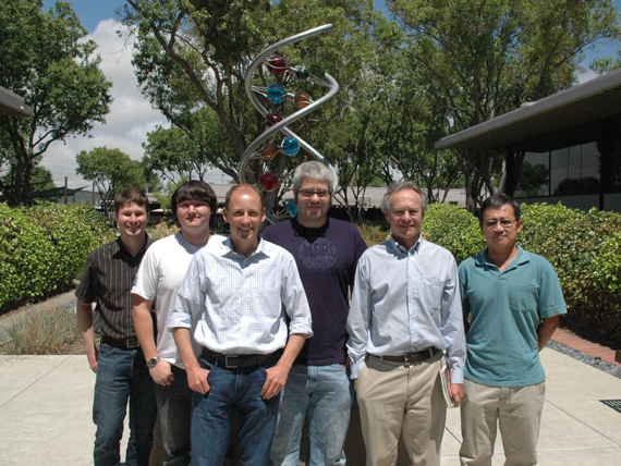 group of people standing in front of a sculpture with bushes and trees behind it