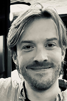 black and white image of a bearded man smiling at the camera