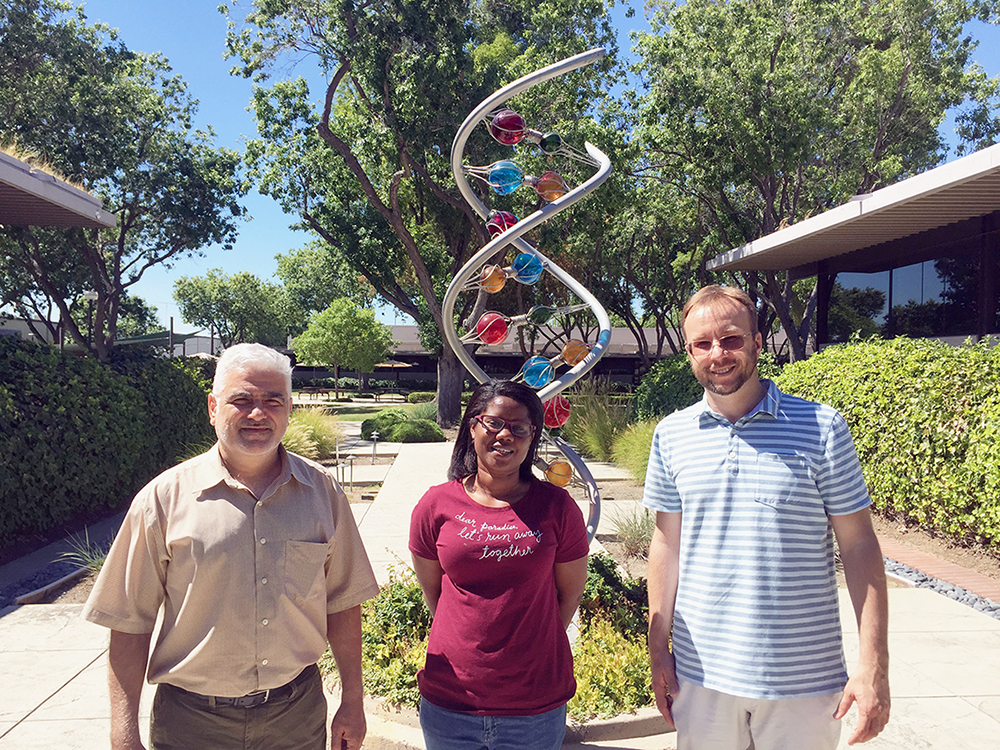 three people standing in front of a statue with trees and bushes surrounding it