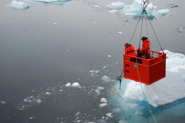 People in a bucket held by a crane over the water