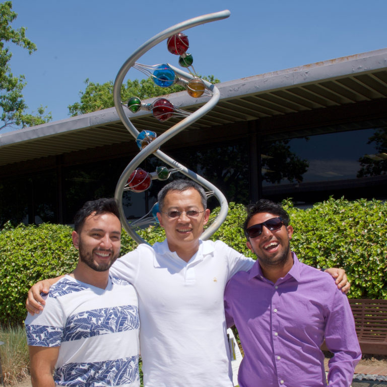 three people with arms around each other in front of a statue