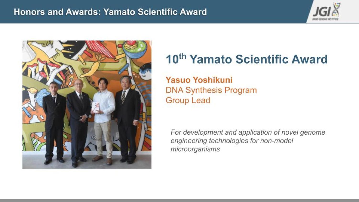 An image of four individuals, one holding a trophy, honors Yasuo Yoshikuni for receiving the 10th Yamamotto Scientific Award