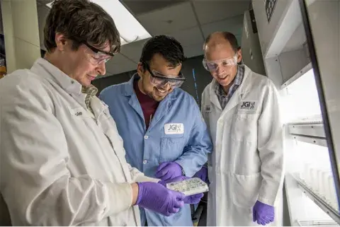 three people in lab gear looking at a box