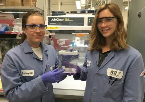 two people in lab gear posing for a photo holding a box