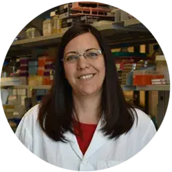 Dark-haired person in a lab coat in a laboratory setting.