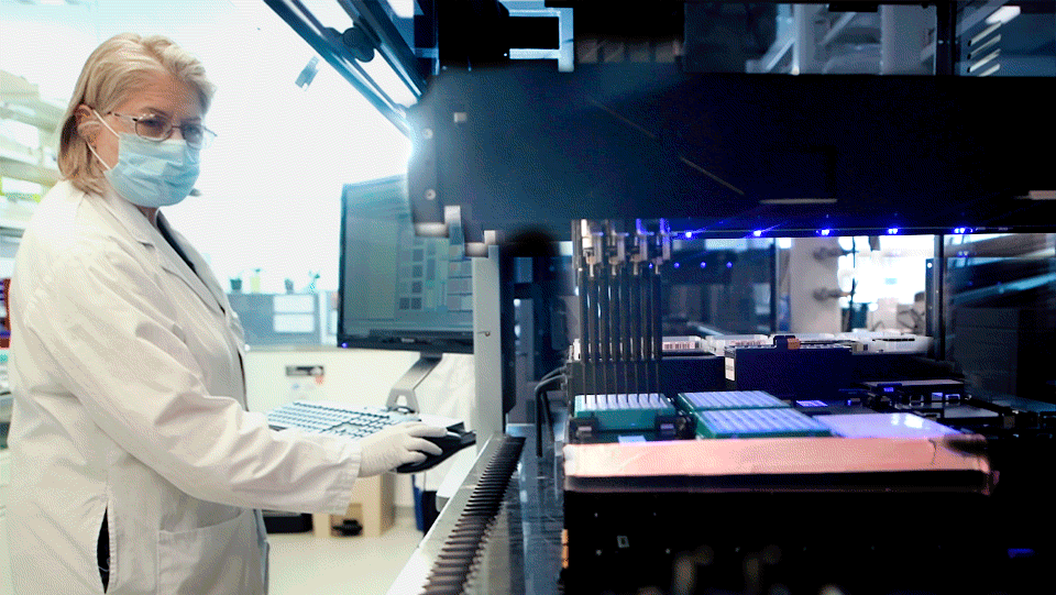 Animated image of Diane Bauer watching a liquid handler processing samples