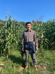 Scientist Xiaosa Jack Xu stands in a field of the plants he studies: corn.