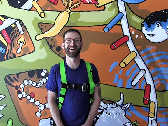 Nigel Sussman smiles as he stands in front of the JGI 25th anniversary mural at the IGB
