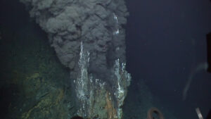 A photo taken in the deep sea. Black clouds billow out of hydrothermal vents.