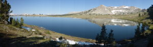 A panoramic view of a lake reflecting a granite mountain.