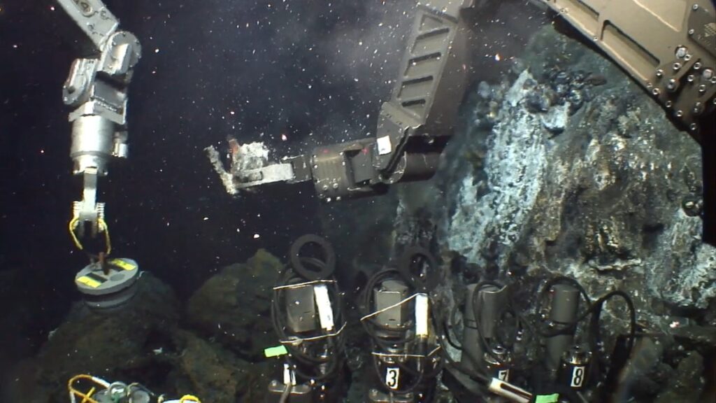 An underwater photo with a robotic arm, moving a sample into a collection canister.
