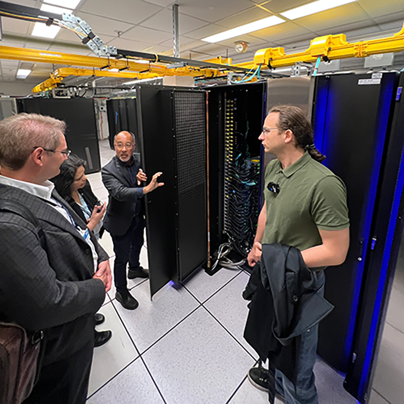 A group of people stands in front of a large black cabinet holding compute nodes.