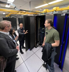 A group of people stands in front of a large black cabinet holding compute nodes.