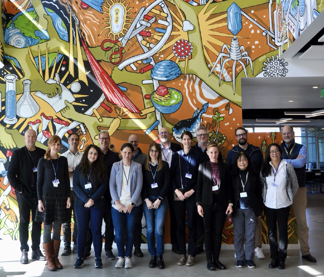 Photo of researchers from University of Duisburg-Essen and the Lawrence Berkeley National Laboratory's Biosciences Area standing in front of the JGI mural in the background.